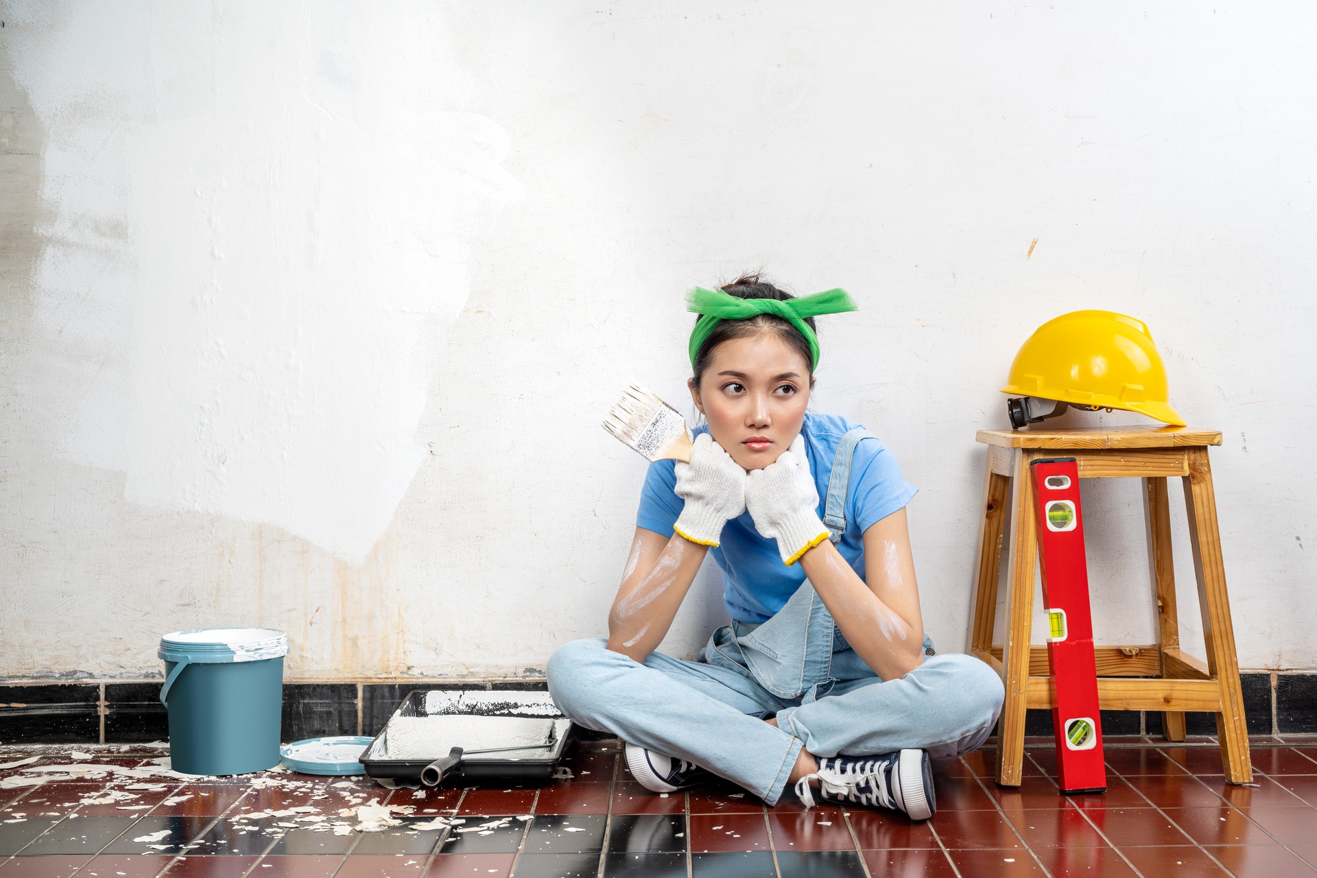 Asian young housewife in a glove holding a paintbrush with an unhappy expression